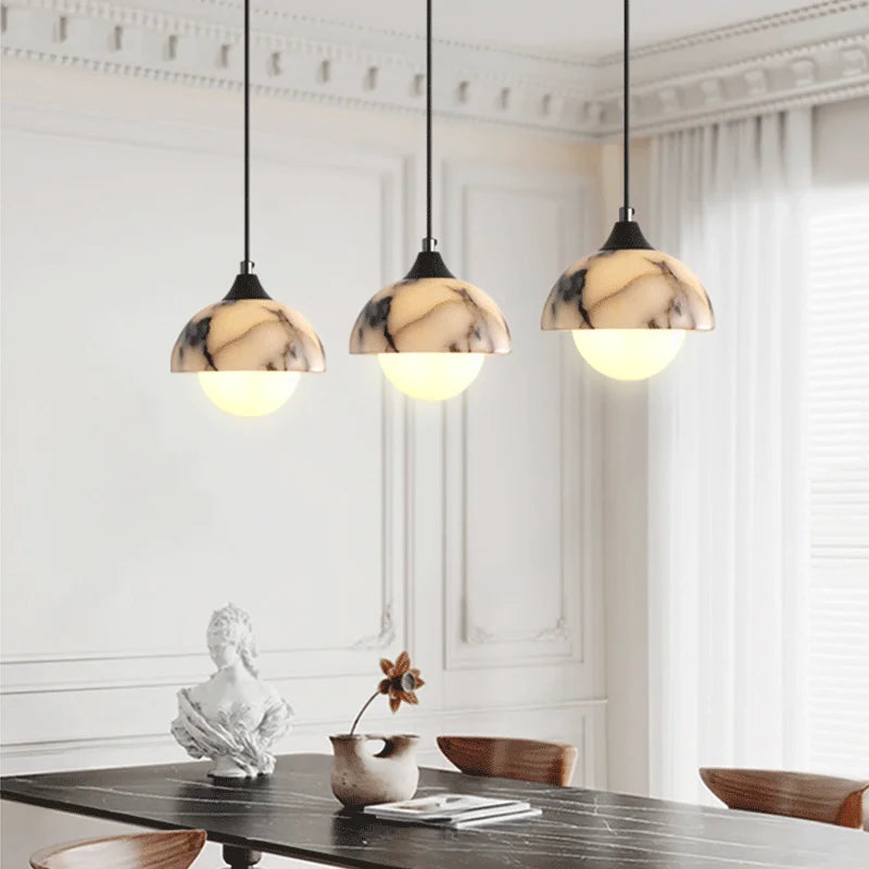 Three pendant lights with marble-like glass shades hanging above a dining table.