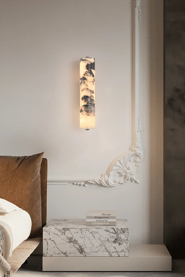 Wall-mounted light fixture in a bedroom setting with a bed and decorative box.