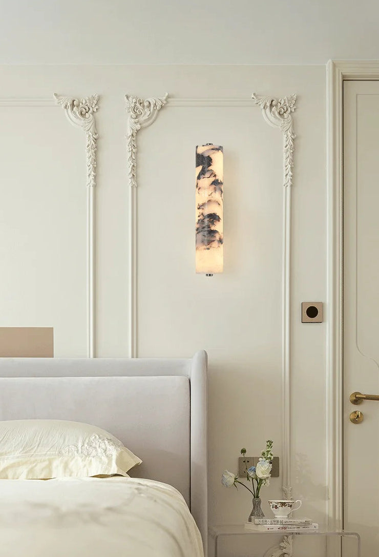 Neatly made bed in a bedroom with decorative wall sconces and a door.