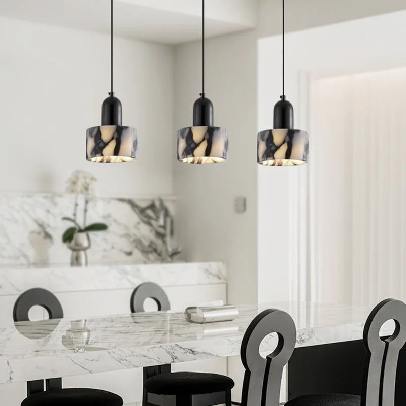 Dining room with marble table and chairs, featuring pendant lights.