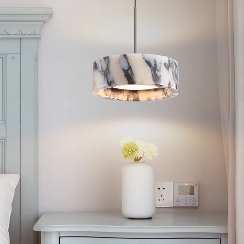 Marble-patterned pendant light above a white vase with flowers on a nightstand.