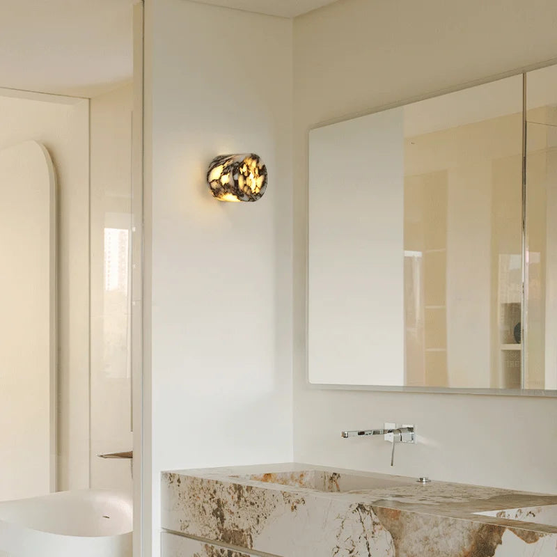 Modern bathroom with marble countertop, mirror, and wall light fixture.