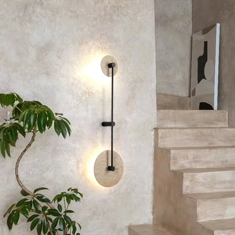 Modern wall sconce on a textured wall with a plant and staircase in the background
