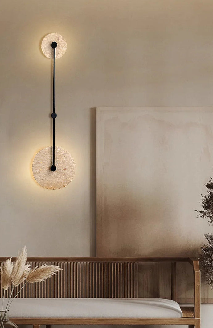 Modern wall light fixture on a neutral wall with a wooden bench and decorative plants.
