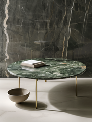 Round marble table with gold legs against a dark marble wall.
